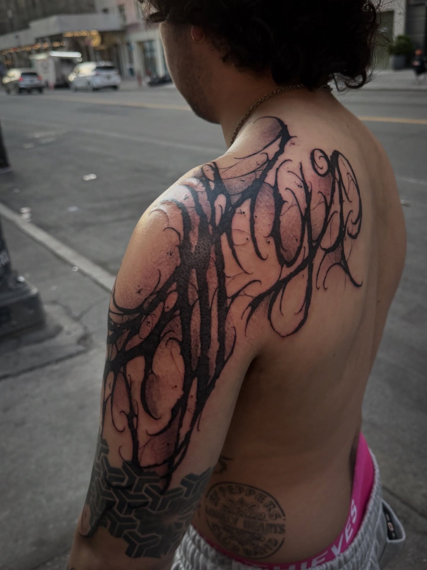 Freehand gothic lettering wrapping the shoulder and upper arm in heavy black strokes with fine hairline flourishes.