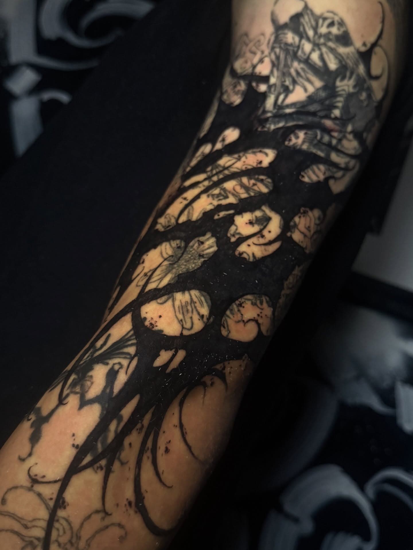 Gothic blackwork blastover on the forearm, with a solid black field and flowing outlines laid over faded older tattoos.