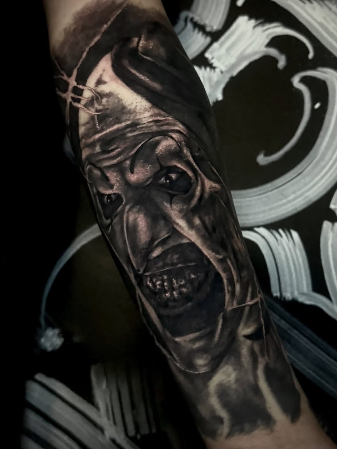 Black-and-grey horror half sleeve centred on a hooded, grinning face with deep shadow and high contrast highlights.