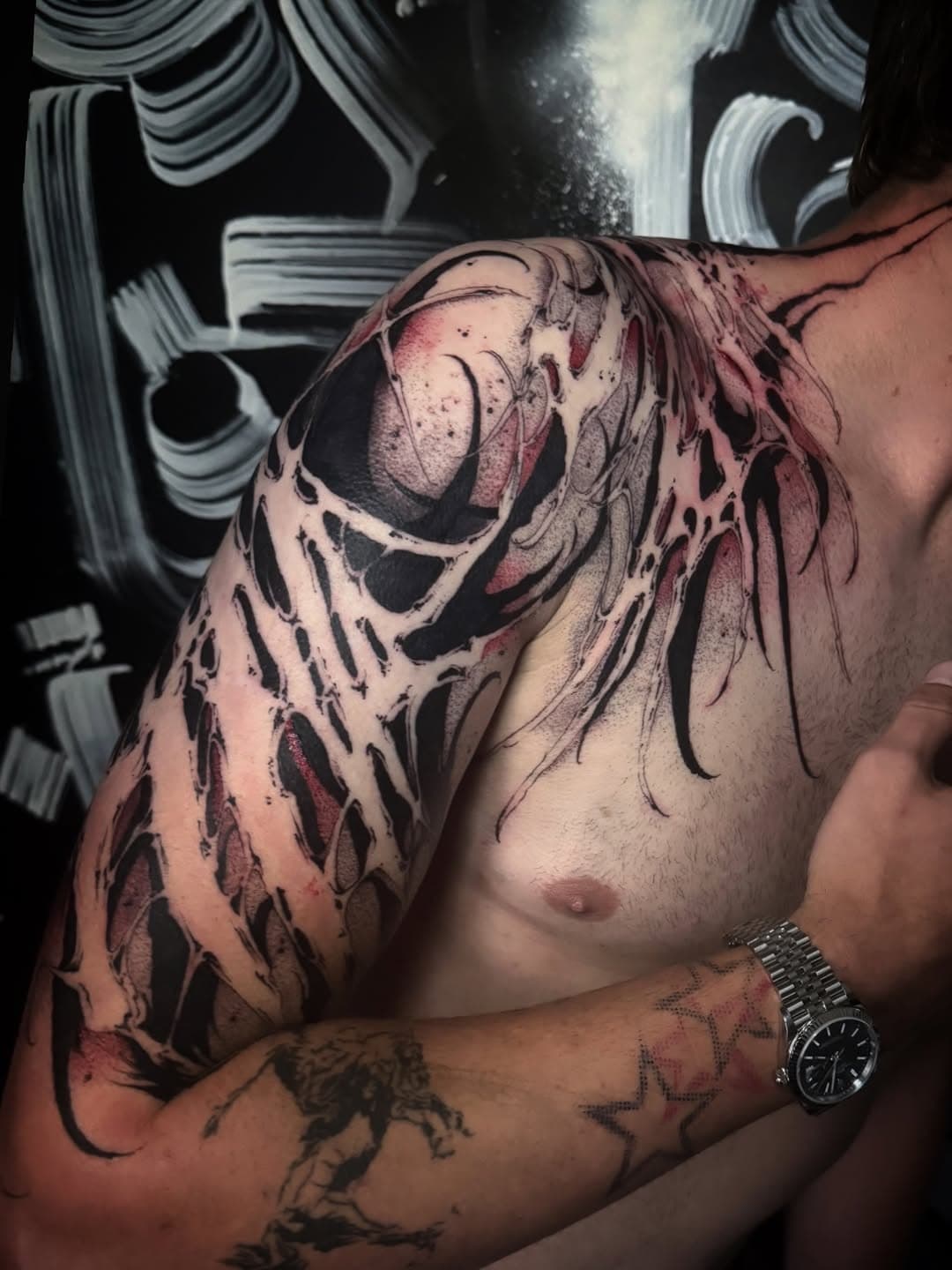 Negative-space blackwork spreading from the shoulder across the chest, with heavy black shapes, red shading and torn organic edges.